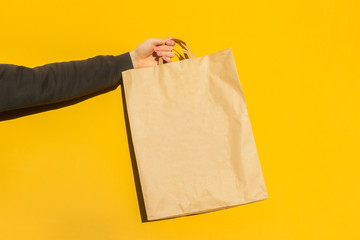 Close up male hold in hand brown empty blank craft paper bag for takeaway on yellow background. Packaging template mockup. food delivery service during coronavirus, concept. Copy space for Advertising