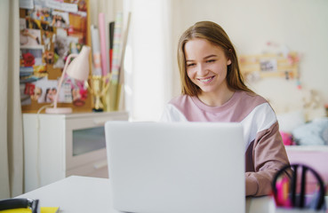 Young female student sitting at the table, using laptop in quarantine.