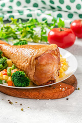 Cooked turkey drumstick with vegetables in a plate on a served table. Baked turkey meat with broccoli, potatoes and carrots.