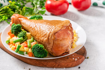 Cooked turkey drumstick with vegetables in a plate on a served table. Baked turkey meat with...
