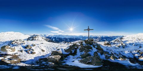 Das sphärische Panorama (360°/180°) zeigt die Rundumsicht vom Karspitz-Gipfel in den Zillertaler Alpen mit Sonnenstern neben dem Gipfelkreuz im Winter.