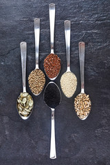 Various Seeds Assortment on dark background. Set of seed: sesame, sunflower, pumpkin, flax, hemp, black cumin in spoons.