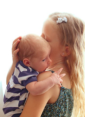 Loving older sister blonde sweetheart touching and gentle holds her newborn brother in her arms, cute tiny baby. The concept of a happy family. Beautiful conceptual of love, trust and tenderness