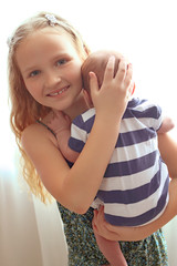 Loving older sister blonde sweetheart touching and gentle holds her newborn brother in her arms,...