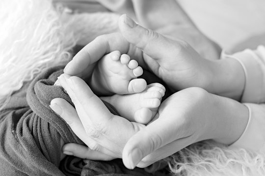 
Black and white photo of the feet of a child in the arms of the mother. Macro shot. Mom and her baby. The concept of a happy family. Beautiful conceptual image of motherhood.