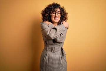 Beautiful arab business woman wearing dress and glasses standing over yellow background Hugging...