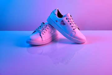 Trendy white teenage sneakers in trendy neon light. Shoe in retro surreal red, blue gradient light....