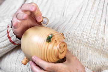 Savings, money, annuity insurance, retirement and people concept - close up of senior man hand putting coin into piggy bank .