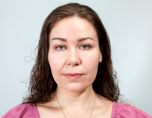 Portrait of a woman with long curly hair with a neutral expression, grey background, emotions...