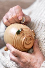 Savings, money, annuity insurance, retirement and people concept - close up of senior man hand putting coin into piggy bank .