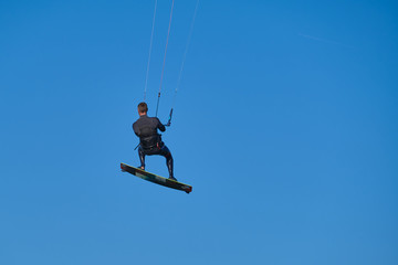 Fototapeta na wymiar Kitesurfer in wetsuit in the jump on a background of blue sky