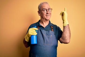 Middle age hoary cleaner man cleaning wearing apron and gloves using sprayer surprised with an idea...
