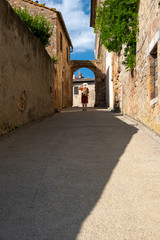a young woman with hat and traveler backpack on a narrow street with an arch on a sunny summer day in Tuscany, Italy