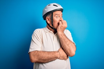 Middle age hoary cyclist man wearing bike security helmet over isolated blue background looking stressed and nervous with hands on mouth biting nails. Anxiety problem.