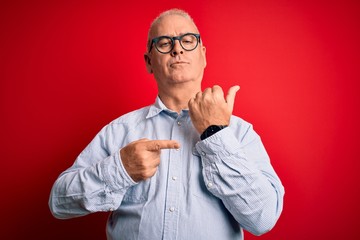 Middle age handsome hoary man wearing casual striped shirt and glasses over red background In hurry...