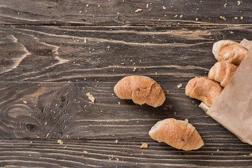 Fresh crispy croissants with chocolate in a paper bag on a wooden background. Top view, copy space. 