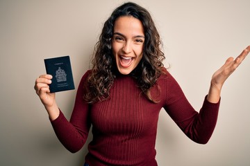 Young beautiful tourist woman with curly hair on vacation holding canadian canada passport very happy and excited, winner expression celebrating victory screaming with big smile and raised hands