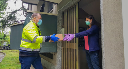 a Courier in protective mask delivers parcel, customer in medical gloves receives box. Delivery service under quarantine, disease outbreak, coronavirus covid-19 pandemic conditions.