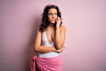 Beautiful woman with curly hair on vacation wearing white swimsuit over pink background looking stressed and nervous with hands on mouth biting nails. Anxiety problem.