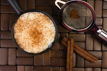 Traditional June party Brazilian dessert made of rice and condensed milk called arroz doce decorated with cinnamon in wood background seen from above