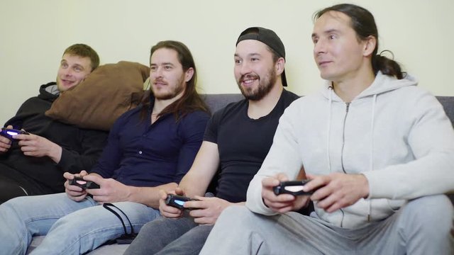 Four guys during the epidemic of coronavirus rest laugh fun, in protective masks playing video games at home