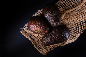 Three avocados and a sack of fique. all in black background