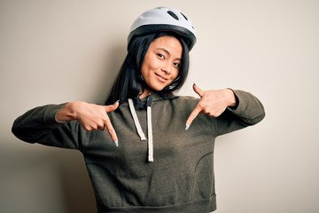 Young beautiful chinese woman wearing bike helmet over isolated white background looking confident with smile on face, pointing oneself with fingers proud and happy.