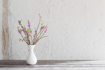 daphne flowers in vase on old wooden table on background white wall