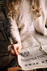 Girl in coat is reading a newspaper while resting in a cafe outdoors