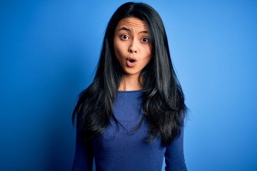 Young beautiful chinese woman wearing casual t-shirt over isolated blue background afraid and shocked with surprise expression, fear and excited face.