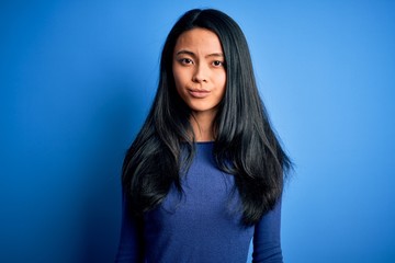 Obraz premium Young beautiful chinese woman wearing casual t-shirt over isolated blue background with serious expression on face. Simple and natural looking at the camera.