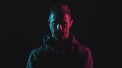 Portrait of computer hacker in hoodie. Obscured dark face in neon light. Data thief, internet fraud, darknet and cyber security.