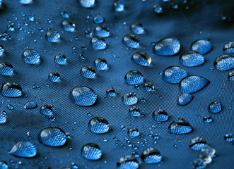 Rain water droplets on blue fiber waterproof fabric. Blue background.