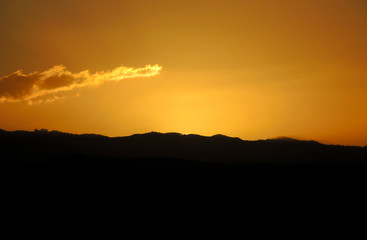 Sun setting or rising behind the top of a hill, outline of a mountain ridge.