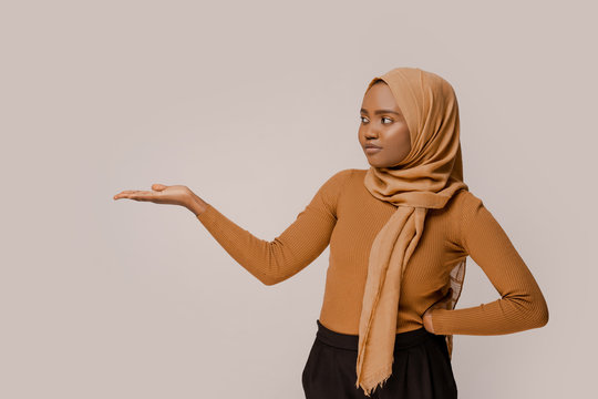 Muslim woman showing copy space for text or logo, presented information. African ethnicity in traditional hijab over white studio background. People and religion. Advertising picture. Smart people