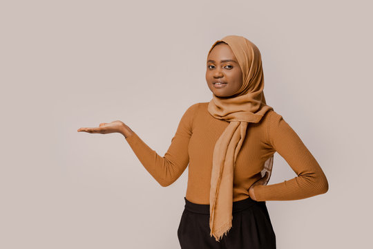 Muslim woman showing copy space and smiling, presented information. African ethnicity in traditional hijab over white studio background. People and religion. Advertising picture