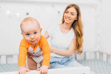 Young beautiful mother, holding a little boy in her arms, sitting on a child's bed, mom woke up with a baby, children's room