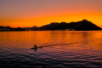 Sunset on Mount Igueldo and and man with a paddle in koyak in Donosti San Sebastian, Basque Country, northern spain