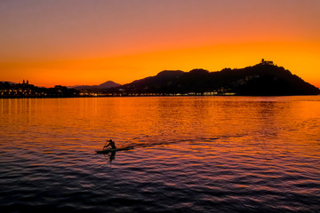 Fototapeta premium Sunset on Mount Igueldo and and man with a paddle in koyak in Donosti San Sebastian, Basque Country, northern spain