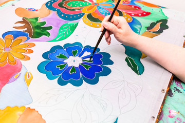 craftsman paints batik with floral pattern on silk