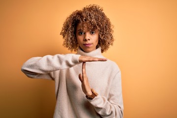 Young beautiful african american woman wearing turtleneck sweater over yellow background Doing time...