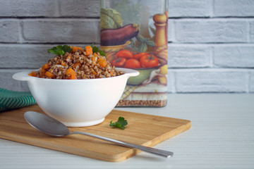 Buckwheat porridge with carrots in a white plate and a glass jar with cereals on a white background and space for copying