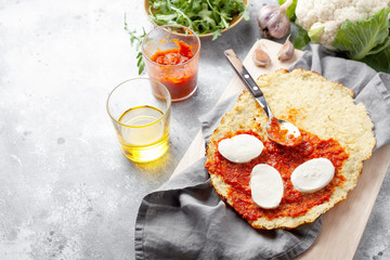 Homemade gluten-free Cauliflower pizza crust dough with tomatoes marinara sauce,mozzarella cheese and arugula on gray background.Vegetable alternative for low-carb and keto diet.Top view,copy space