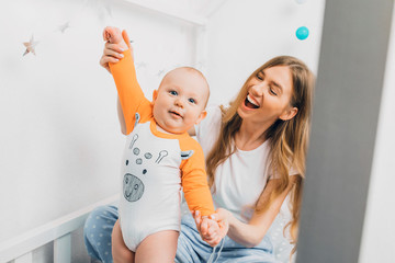 Mother and child on a white bed. Mom and baby boy are playing. A parent and a small child are...