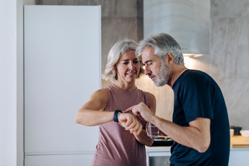Mature couple using smartwatch in kitchen at home