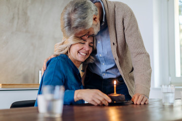 Mature couple celebrating birthday with cake in kitchen at home