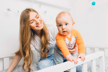 Mother and child on a white bed. Mom and baby boy are playing. A parent and a small child are resting at home. Family has fun together