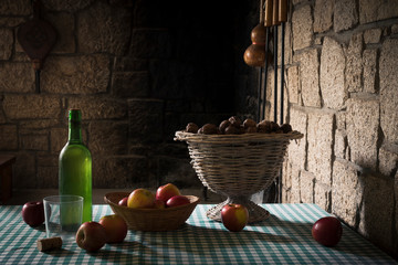 Bodegón con una botella de vino blanco, manzanas  y una cesta de nueces sobre una mesa con mantel a cuadros azules y fondo oscuro