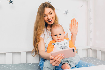 mother and a small baby relax while sitting on the bed and take a selfie on their mobile phone.