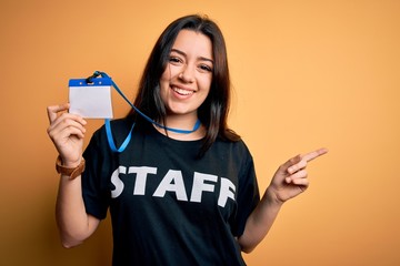 Young brunette worker woman wearing staff t-shirt as uniform showing id card very happy pointing...